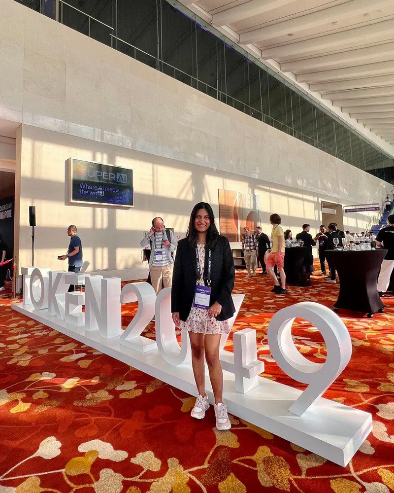 Shilika Jain in a black blazer beside the TOKEN2049 Singapore sign in the conference hall